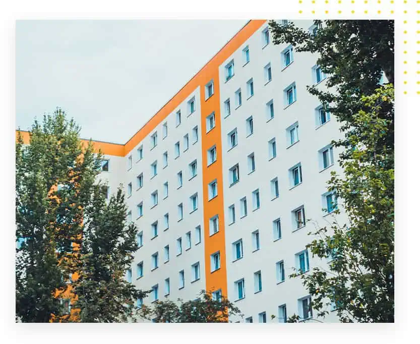 Mehrfamilienhaus mit orangefarbenem Akzent und weißen Wänden, umgeben von Bäumen und Fenstern in verschiedenen Größen.