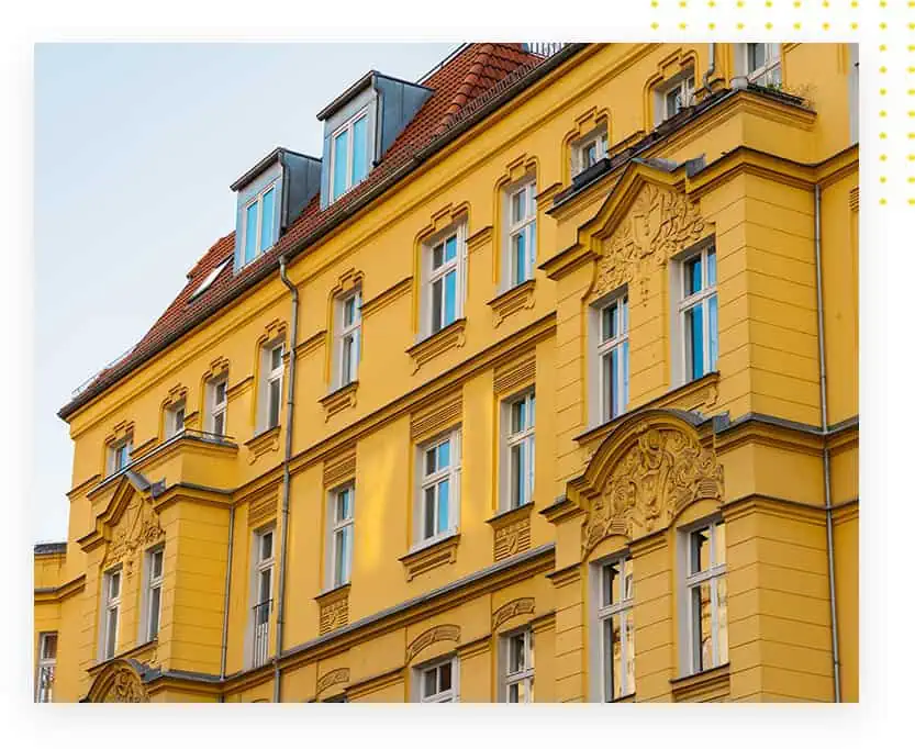 Gelbes Gebäude mit kunstvollen Fassadendetails und Fenstern im oberen Bereich, das architektonische Merkmale des Denkmalschutzes zeigt.